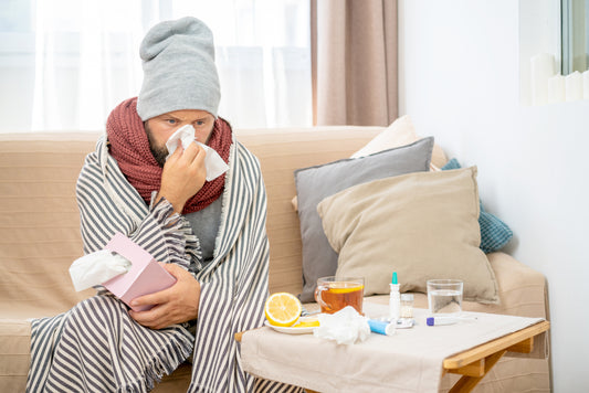 Mies flunssassa sohvalla nenäliinapaketti kädessään